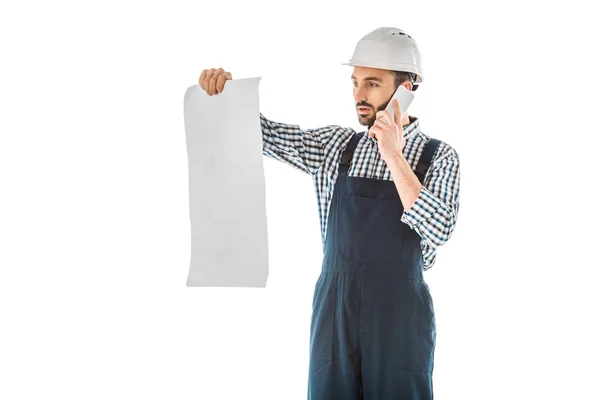 Attentive construction worker talking on smartphone while looking at building plan isolated on white — Stock Photo