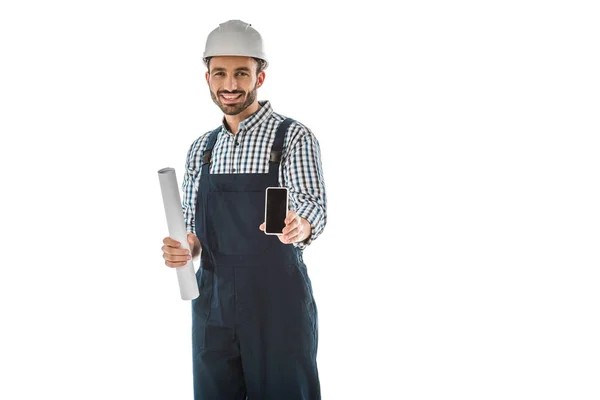 Cheerful construction worker holding smartphone with blank screen and looking at camera isolated on white — Stock Photo