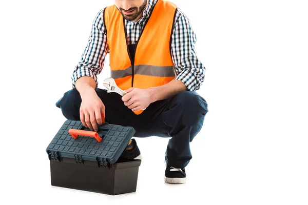 Vista parcial del trabajador de la construcción consiguiendo llave ajustable de la caja de herramientas aislada en blanco - foto de stock