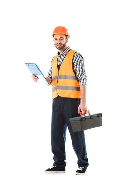 Alegre trabajador de la construcción sosteniendo caja de herramientas y portapapeles aislados en blanco - foto de stock