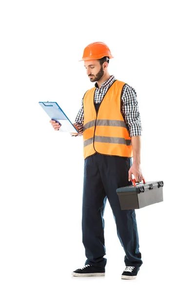 Trabajador serio de la construcción sosteniendo caja de herramientas y mirando el portapapeles aislado en blanco - foto de stock