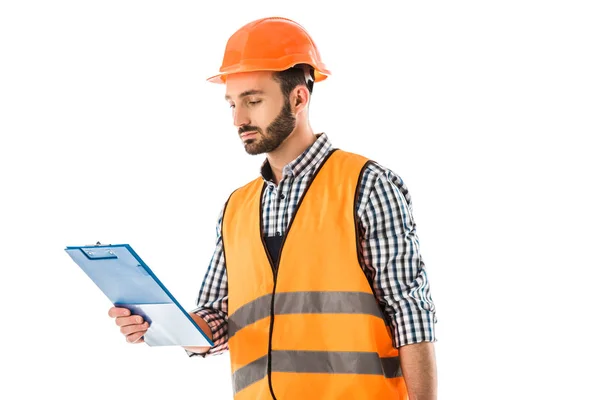 Serious construction worker in safety vest and helmet looking at clipboard isolated on white — Stock Photo