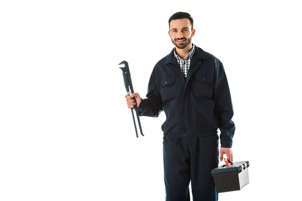 Cheerful plumber in overalls holding adjustable wrench and toolbox isolated on white — Stock Photo