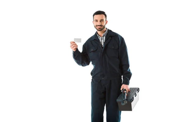 Smiling workman in overalls holding toolbox and blank business card isolated on white — Stock Photo