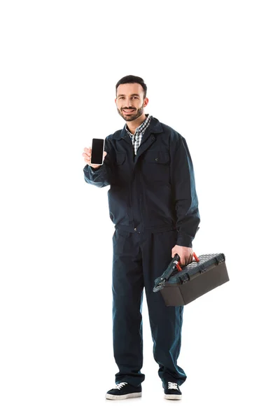 Handyman alegre com caixa de ferramentas segurando smartphone com tela em branco e olhando para a câmera isolada no branco — Fotografia de Stock
