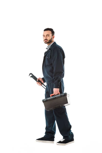 Serious plumber holding adjustable wrench and toolbox isolated on white — Stock Photo