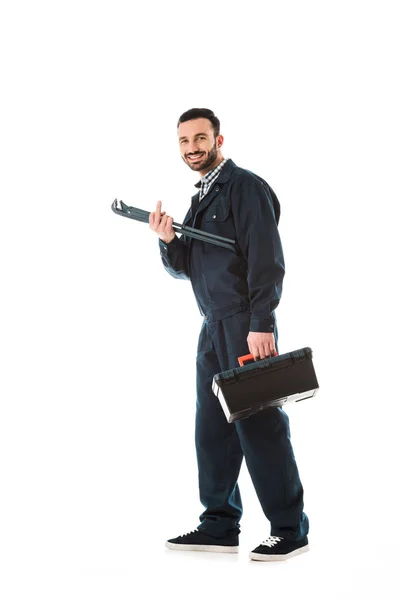 Cheerful plumber with toolbox and adjustable wrench showing middle finger while smiling at camera isolated on white — Stock Photo
