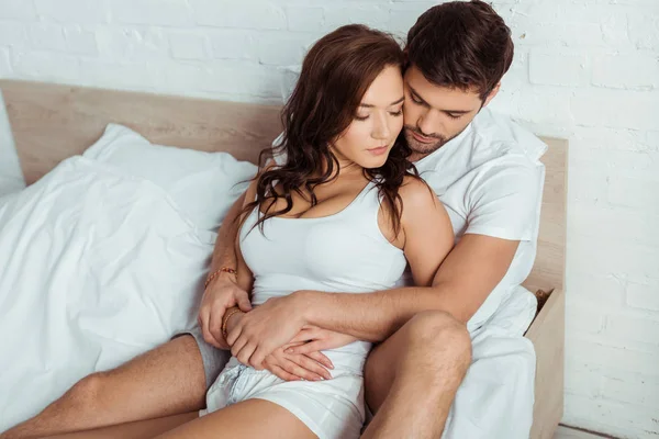 Overhead view of man hugging attractive woman while lying on bed — Stock Photo