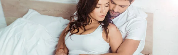 Tiro panorâmico de homem abraçando mulher atraente enquanto deitado na cama — Fotografia de Stock