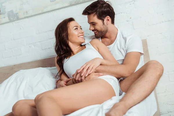 Hombre guapo acostado en la cama con novia alegre en el dormitorio — Stock Photo