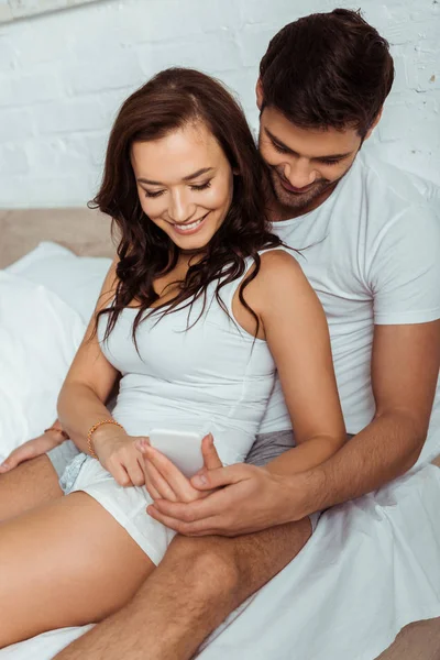 Glückliche Frau mit Smartphone im Bett mit Mann — Stockfoto
