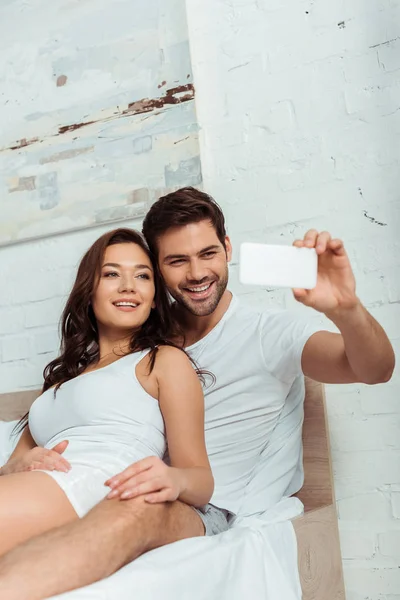 Homem feliz sorrindo perto de namorada atraente ao tomar selfie — Fotografia de Stock