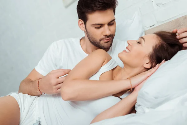 Красивый мужчина смотрит на улыбающуюся девушку, лежа на кровати — стоковое фото