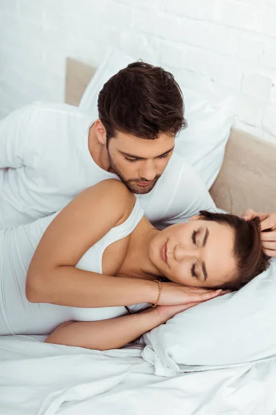 Handsome man looking at attractive girl lying on bed with closed eyes — Stock Photo