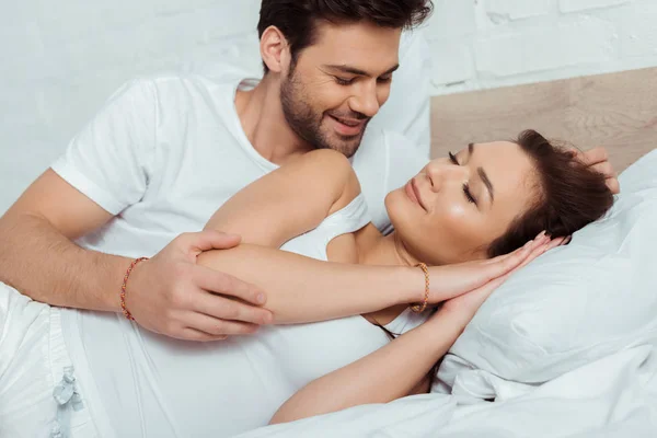 Щасливий чоловік дивиться на привабливу дівчину, що лежить на ліжку з закритими очима — стокове фото