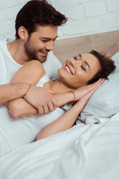 Alegre hombre mirando feliz chica acostado en la cama con los ojos cerrados - foto de stock