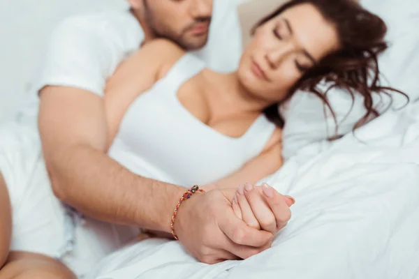 Enfoque selectivo de pareja cogida de la mano mientras está acostada en el dormitorio - foto de stock