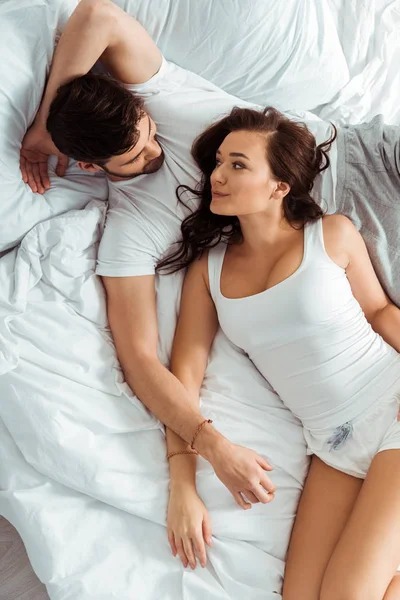 Top view of handsome man looking at attractive woman while lying on bed — Stock Photo