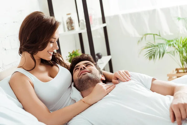 Feliz novia mirando novio acostado en la cama - foto de stock