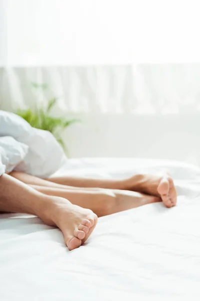 Обрезанный вид босиком на лежащих на кровати мужчин и молодых женщин — стоковое фото