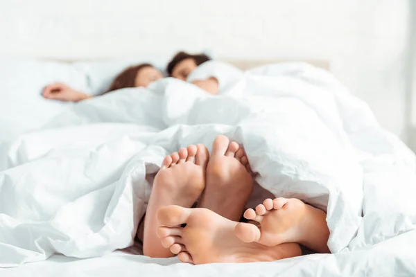 Selective focus of barefoot of young woman and man lying under blanket in bed — Stock Photo
