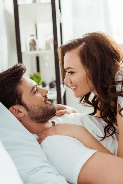 Mulher feliz olhando para namorado bonito enquanto deitado no quarto — Fotografia de Stock