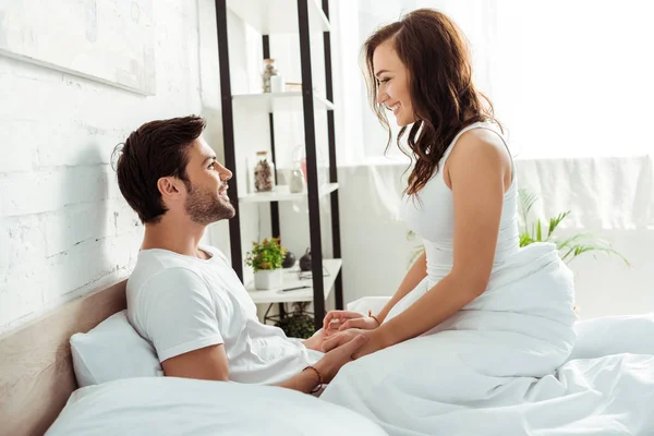 Glückliche junge Frau schaut Freund an, während sie auf dem Bett sitzt — Stockfoto