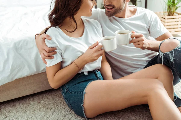 Обрезанный вид мужчины и веселой женщины с чашками кофе в спальне — стоковое фото