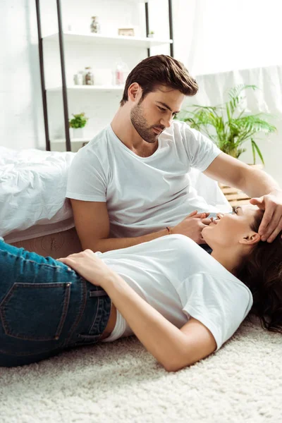 Bel homme regardant jolie fille couchée sur le tapis dans la chambre — Photo de stock