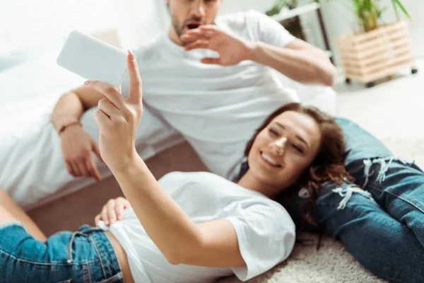 Selective focus of cheerful girl taking selfie with man in bedroom — Stock Photo