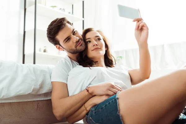 Baixo ângulo de visão de homem e mulher tomando selfie no quarto — Fotografia de Stock