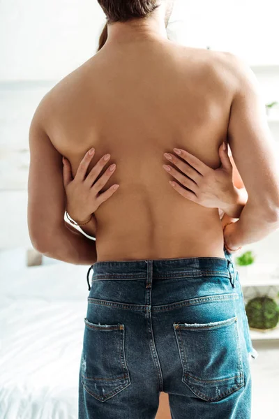 Cropped view of woman hugging shirtless muscular man in bedroom — Stock Photo