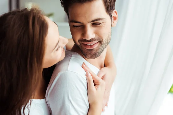 Attraente ragazza abbracciare felice uomo in piedi in bianco t-shirt a casa — Foto stock