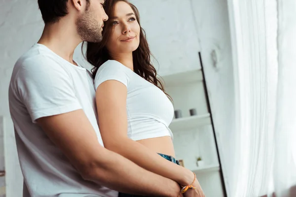 Low angle view of man hugging smiling woman in white t-shirt at home — Stock Photo