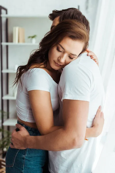 Novio abrazando atractiva novia con los ojos cerrados en casa - foto de stock