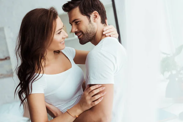 Hombre feliz mirando a chica alegre mientras se abraza en casa - foto de stock