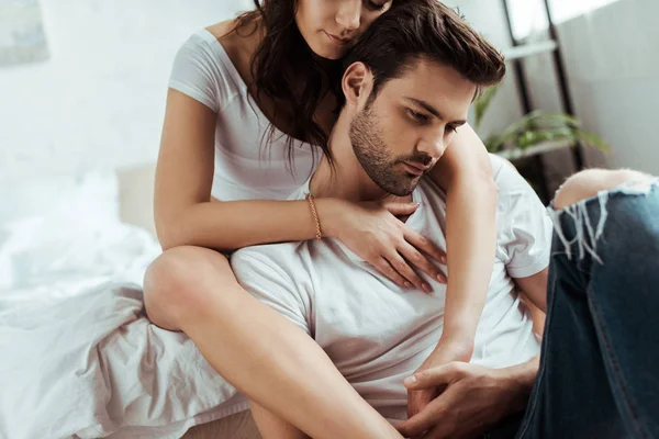 Обрезанный вид женщины, сидящей на кровати и обнимающей красивого мужчину — стоковое фото