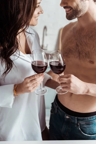 Vista recortada de hombre musculoso alegre sosteniendo copa de vino cerca de chica atractiva en casa - foto de stock