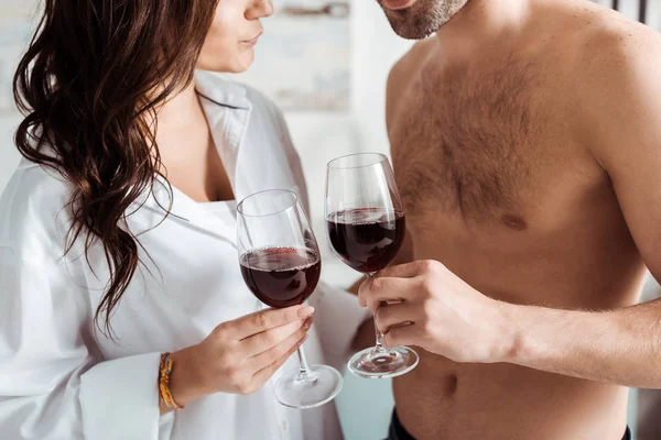 Corte vista de muscular homem e morena menina segurando copos de vinho em casa — Fotografia de Stock