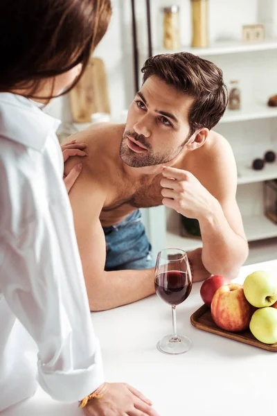 Selective focus of brunette girl looking at handsome muscular man in kitchen — Stock Photo