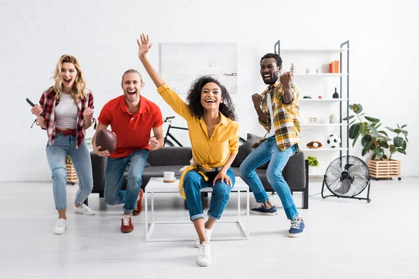 Riendo amigos multiculturales regocijándose en la sala de estar en casa - foto de stock