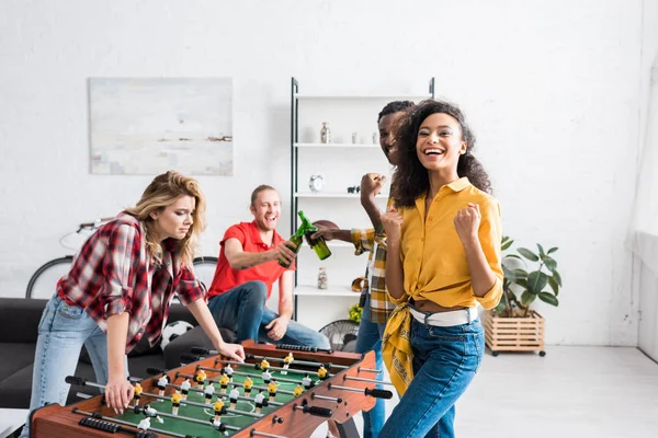 Glückliche und lächelnde multiethnische Männer und Frauen beim Tischkicker im heimischen Wohnzimmer — Stockfoto