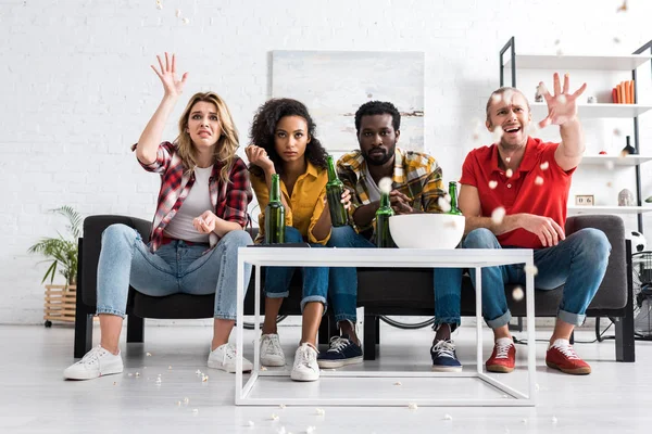 Four displeased multiethnic friends sitting on couch, watching movie and throwing popcorn — Stock Photo
