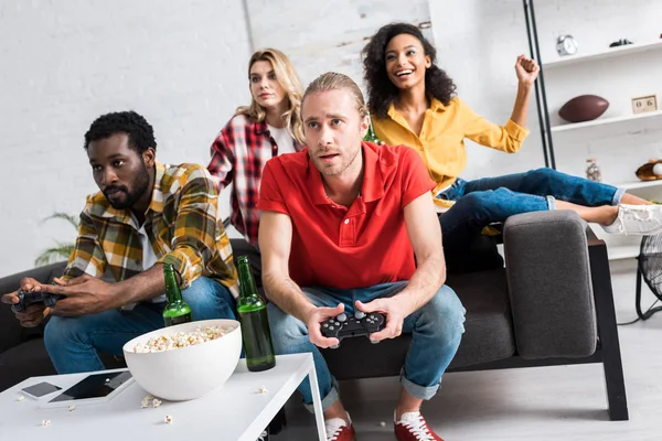 Selective focus of multicultural men playing video game near girls at home — Stock Photo