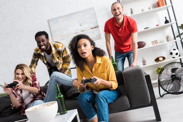 Low angle view of happy multicultural girls playing video game near friends — Stock Photo