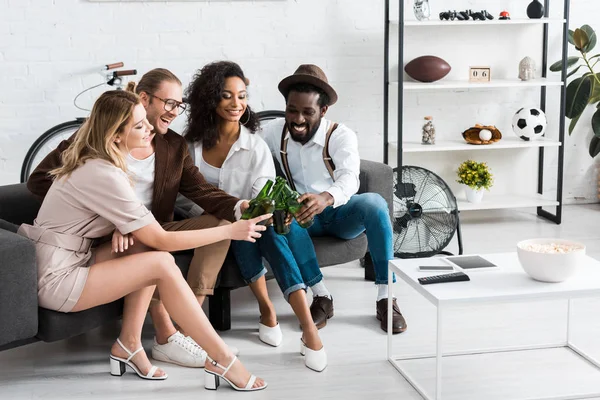 Alegres hombres multiculturales tostadas con mujeres atractivas en la sala de estar - foto de stock