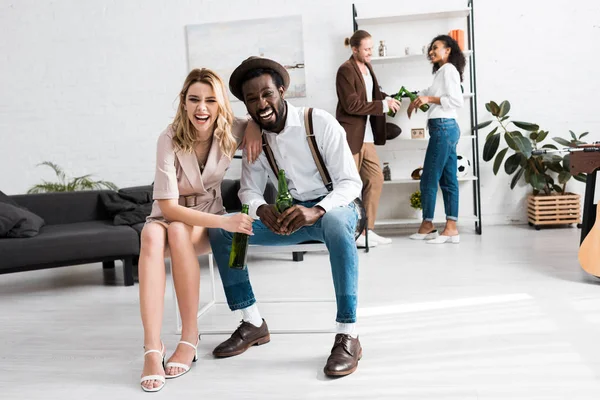 Selektiver Fokus eines glücklichen Mädchens, das mit einem fröhlichen afrikanisch-amerikanischen Mann lacht, der eine Flasche Bier hält — Stockfoto