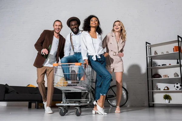 Vista de ángulo bajo del hombre afroamericano guapo en el carrito de compras cerca de amigos felices - foto de stock