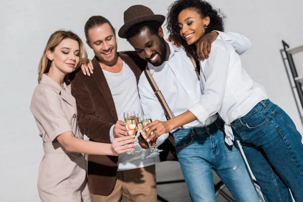 Low angle view of happy multicultural friends smiling while clinking champagne glasses — Stock Photo
