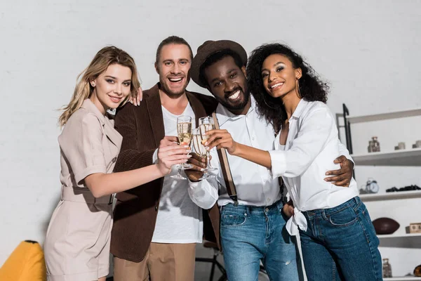 Vista de ángulo bajo de alegres amigos multiculturales sonriendo mientras tintinean copas de champán - foto de stock